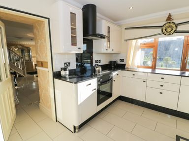 A kitchen with white cabinets black countertops an oven a kettle and a window at Bryn Berthen in Penrhyndeudraeth