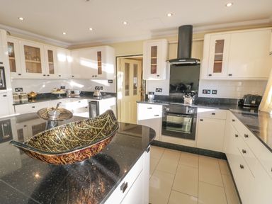 A kitchen with black countertops white cabinets an oven and a decorative bowl on an island at Bryn Berthen in Penrhyndeudraeth