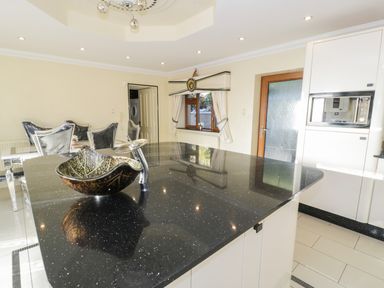 A kitchen with a black countertop island and silver chairs around a dining table at Bryn Berthen in Penrhyndeudraeth