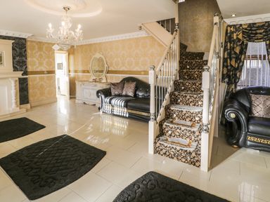 A living room with black sofas patterned stairs rugs a chandelier and an ornate sideboard at Bryn Berthen in Penrhyndeudraeth