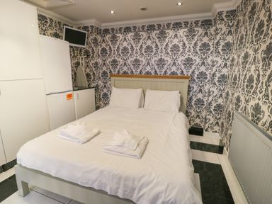 A bedroom with a double bed two folded towels a radiator white cupboards and a wall-mounted television at Bryn Berthen in Penrhyndeudraeth