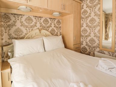 A bedroom with a bed with white bedding and pillows wardrobes and patterned wallpaper at Bryn Berthen in Penrhyndeudraeth