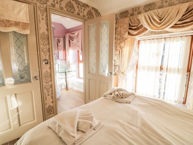 A bedroom with a bed and folded towels near an open door leading to a bathroom with a glass sink and window at Bryn Berthen in Penrhyndeudraeth
