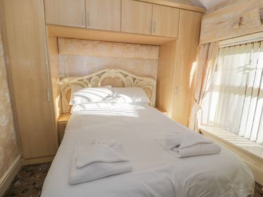 A bedroom with a double bed white linens folded towels built in wardrobes and a window with vertical blinds at Bryn Berthen in Penrhyndeudraeth
