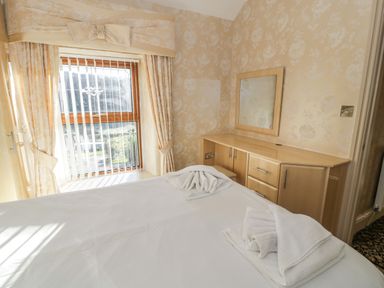 A bedroom with a bed and folded towels near a window and a wooden vanity unit with a mirror at Bryn Berthen in Penrhyndeudraeth
