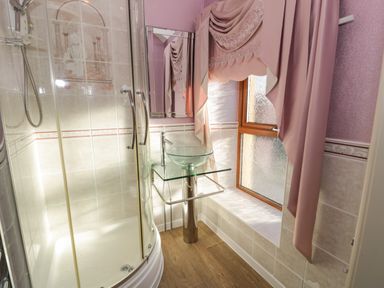 A bathroom with a glass shower enclosure a glass sink and pink curtains at Bryn Berthen Penrhyndeudraeth