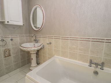 A bathroom with a pedestal sink mirror bathtub and tiled walls at Bryn Berthen in Penrhyndeudraeth