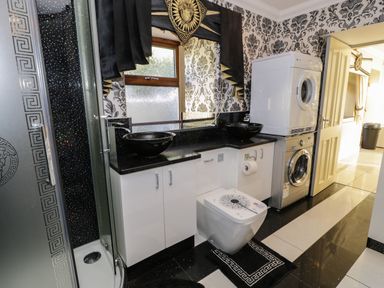 A bathroom with a shower cabin a toilet two black sinks washing machine and dryer at Bryn Berthen in Penrhyndeudraeth