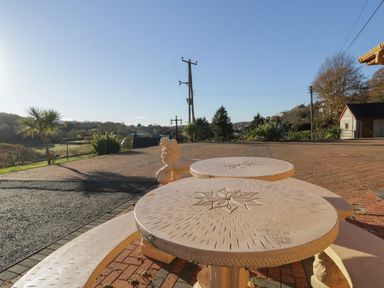 An outdoor area with round stone tables and a lion sculpture near a brick paved driveway at Bryn Berthen in Penrhyndeudraeth
