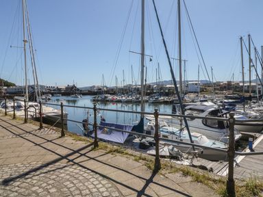 A marina with sailboats docked along a paved walkway and buildings in the background at Bryn Berthen in Penrhyndeudraeth