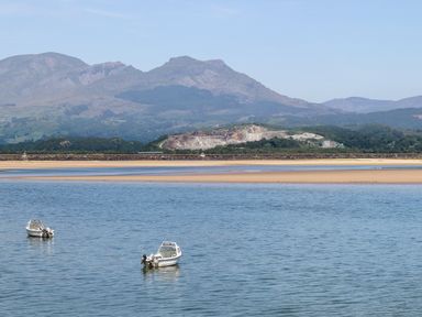 Two small boats on water with sandy shore and mountains in the background at Bryn Berthen in Penrhyndeudraeth
