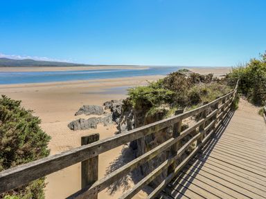 A wooden boardwalk with railings leading to a sandy beach with rocks and water at Bryn Berthen in Penrhyndeudraeth