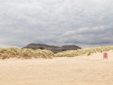 A sandy beach with tall grass dunes and mountains in the background at Bryn Berthen in Penrhyndeudraeth