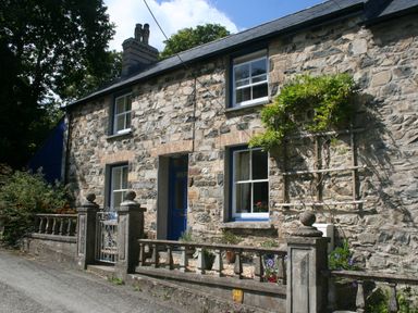 Stone house with blue door and windows and a small front garden with a stone fence at Delfryn Newport