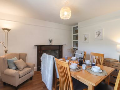 A dining room with a wooden table set for breakfast and an armchair near a fireplace at Delfryn Newport