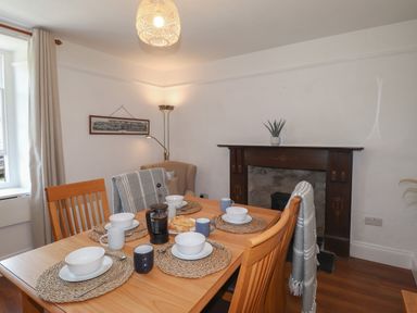 A dining room with a wooden table set for four and a fireplace with a plant at Delfryn Newport in Newport Pembrokeshire