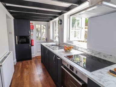 A kitchen with marble countertops dark cabinets an electric hob and oven a sink with a window above it and a door at Delfryn Newport in Newport Pembrokeshire