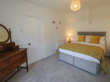 A bedroom with a double bed with yellow pillows and throw a wooden dresser and a door at Delfryn Newport in Newport Pembrokeshire