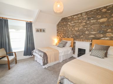 A bedroom with two single beds a stone wall and a window with blue curtains at Delfryn Newport in Newport Pembrokeshire