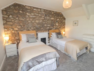 A bedroom with two single beds a stone wall and bedside tables with lamps at Delfryn Newport Newport Pembrokeshire