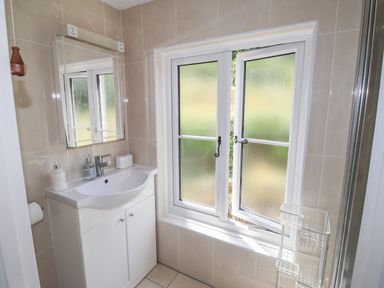A bathroom with a white sink cabinet a mirror above and frosted glass windows at Delfryn Newport in Newport Pembrokeshire