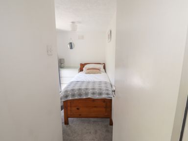 A small bedroom with a single wooden bed a white chest of drawers and a gray lamp at Delfryn Newport in Newport Pembrokeshire