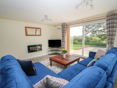 A living room with blue couches a wooden coffee table and a TV near a sliding glass door at Erwlon in Rhydyfelin near Aberystwyth