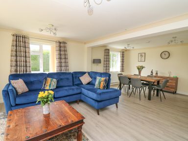 A living room with a blue sectional sofa and wooden coffee table with flowers at Erwlon in Rhydyfelin near Aberystwyth