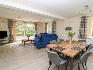 A living room with blue sofas a wooden dining table with chairs and flowers on it at Erwlon in Rhydyfelin near Aberystwyth