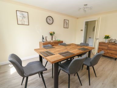 A dining room with wooden table and six gray chairs near two wooden sideboards with flowers and decorations at Erwlon in Rhydyfelin near Aberystwyth