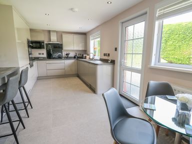 A kitchen with grey cabinets bar stools glass table and chairs at Erwlon in Rhydyfelin near Aberystwyth