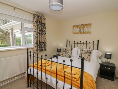 A bedroom with a black metal bed frame two bedside tables with lamps and floral curtains at Erwlon in Rhydyfelin near Aberystwyth