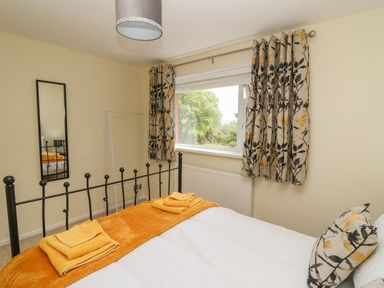 A bedroom with a bed folded towels a window with floral curtains and a full length mirror at Erwlon Rhydyfelin near Aberystwyth
