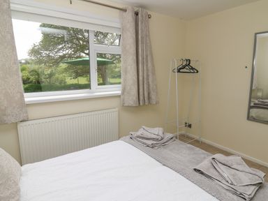 A bedroom with a bed folded towels on the bed a window with curtains a radiator a clothing rack and a wall mirror at Erwlon in Rhydyfelin near Aberystwyth
