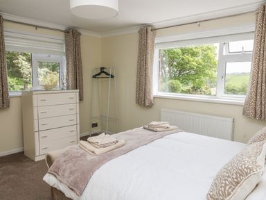 A bedroom with a bed towels on top a chest of drawers and windows with curtains at Erwlon in Rhydyfelin near Aberystwyth