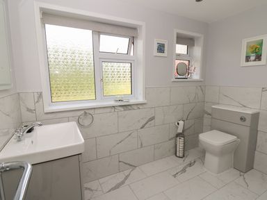 A bathroom with a sink a toilet two windows and tiled walls and floor at Erwlon in Rhydyfelin near Aberystwyth