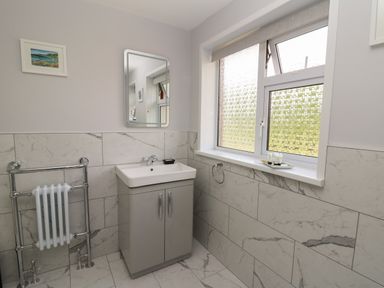 A bathroom with a sink cabinet mirror towel radiator and frosted window at Erwlon in Rhydyfelin near Aberystwyth
