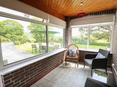 A sunroom with two chairs and a table overlooking a garden with outdoor furniture at Erwlon in Rhydyfelin near Aberystwyth