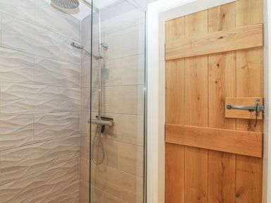 A shower area with textured tiles and a wooden door with a latch at Fron Olau in Nefyn