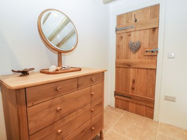 A wooden dresser with a round mirror and seashells on top next to a wooden door with a heart decoration at Fron Olau in Nefyn