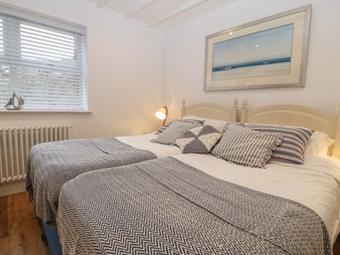 A bedroom with two single beds pushed together with striped pillows and blankets and a window with blinds at Fron Olau in Nefyn