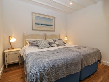 A bedroom with a double bed with striped pillows and blankets two bedside tables with lamps a painting on the wall at Fron Olau in Nefyn