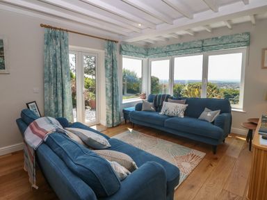 A sitting room with two blue sofas and large windows overlooking a garden at Fron Olau in Nefyn