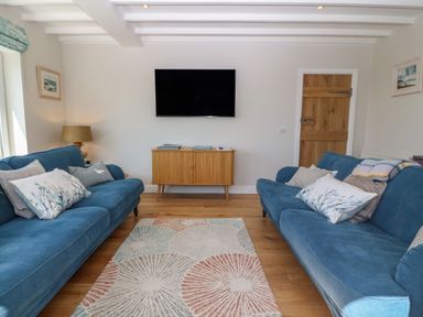 A living room with two blue sofas a wooden cabinet a wall-mounted tv and a patterned rug at Fron Olau in Nefyn