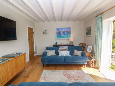 A living room with blue sofas a rug wooden floor paintings and a cabinet at Fron Olau in Nefyn