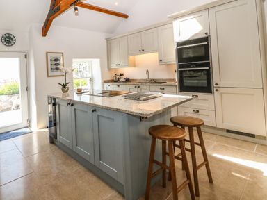 A kitchen with an island with two wooden stools and cabinets at Fron Olau in Nefyn