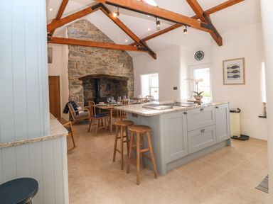 A kitchen with an island and stools a dining table with chairs and a stone fireplace at Fron Olau in Nefyn