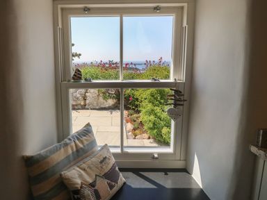 A window with cushions on the sill overlooking a garden and sea at Fron Olau in Nefyn