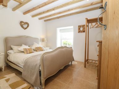 A bedroom with a bed a bedside table with a lamp a window and a wooden clothes rack at Fron Olau in Nefyn