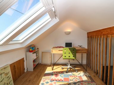 A small attic workspace with a wooden desk green chair colorful rug and skylight window at Fron Olau in Nefyn